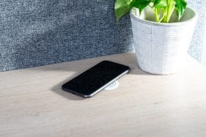 ARC 44 wireless charger in black charging a phone next to a potted plant on a desk