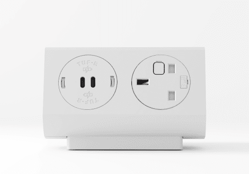 White wall-mounted power outlet featuring two circular sockets side by side on a white base. Left socket shows two vertical slots with green indicators; right socket has a different receptacle opening and a fuse label.