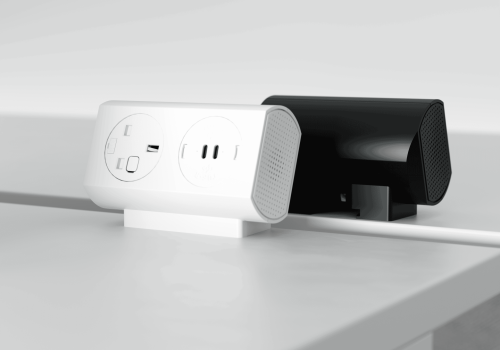 Close-up of a white power strip with outlets on a desk, next to a black device with mesh sides